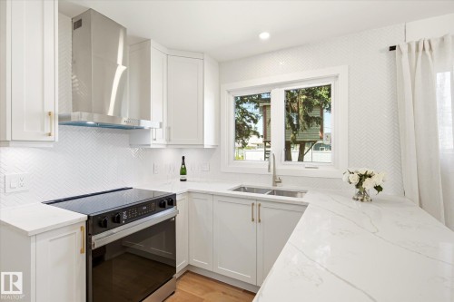 Modern kitchen featuring white shaker cabinetry, gold-finish hardware, a stainless steel range hood, stone countertops, and a herringbone tile backsplash - 4708 104A Avenue Nw, Edmonton, AB - Indoor Photo Showing Kitchen With Double Sink With Upgraded Kitchen