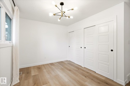 Room featuring wood-finish flooring, a contemporary chandelier, white walls, and a window - 4708 104A Avenue Nw, Edmonton, AB - Indoor Photo Showing Other Room