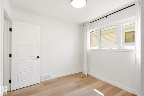 Room featuring wood-finish flooring, a white five-panel door with black hardware, a three-pane window with white trim, a black curtain rod, and a flush-mount ceiling light fixture - 4708 104A Avenue Nw, Edmonton, AB - Indoor Photo Showing Other Room