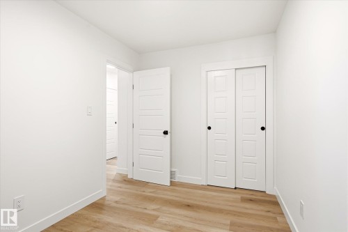 Bright interior room featuring wood-finish flooring, white walls, and a white sliding closet door - 4708 104A Avenue Nw, Edmonton, AB - Indoor Photo Showing Other Room