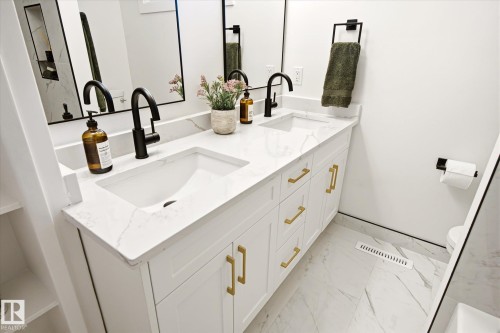 Dual vanity with integrated sinks, white cabinetry, gold-finish hardware, black-finish faucets, and patterned flooring - 4708 104A Avenue Nw, Edmonton, AB - Indoor Photo Showing Bathroom