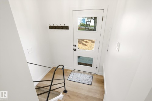 Entryway featuring a white door with three square lites, light wood-finish flooring, a black metal handrail, and a dark wall-mounted coat rack - 4708 104A Avenue Nw, Edmonton, AB - Indoor Photo Showing Other Room