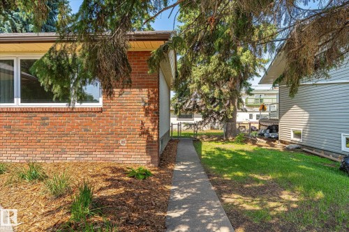 Brick exterior with white frame windows, featuring a concrete walkway, mulched landscaping, and established trees - 4708 104A Avenue Nw, Edmonton, AB - Outdoor