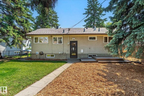Rear exterior featuring an elevated multi-level deck, concrete walkway, and a mix of lawn and wood mulch landscaping - 4708 104A Avenue Nw, Edmonton, AB - Outdoor