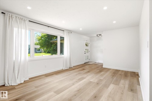 Open-concept living area featuring wood-finish flooring, recessed lighting, and a white paneled entry door with frosted glass inserts - 4708 104A Avenue Nw, Edmonton, AB - Indoor Photo Showing Other Room