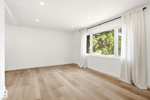 Spacious room featuring light wood-finish flooring, recessed lighting, and a large multi-pane window with white trim - 4708 104A Avenue Nw, Edmonton, AB - Indoor Photo Showing Other Room