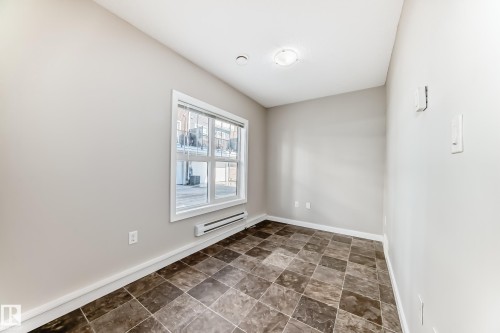 Neutral wall color, window with white trim, brown and tan patterned tile flooring, and a ceiling-mounted light fixture - #75 2803 James Mowatt Tr Sw, Edmonton, AB 