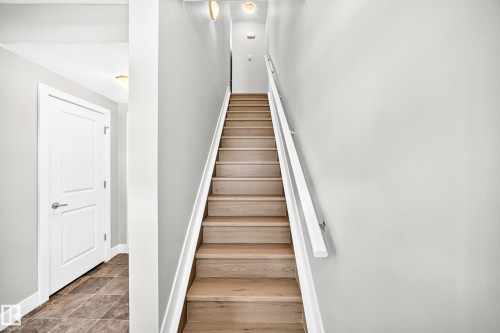Wood-finish staircase with white handrail, recessed wall lighting, and neutral wall tones - #75 2803 James Mowatt Tr Sw, Edmonton, AB 