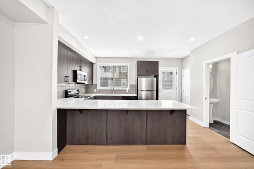 Kitchen featuring dark wood-finish cabinetry, stainless steel appliances, a white countertop island, and wood-finish flooring - #75 2803 James Mowatt Tr Sw, Edmonton, AB 