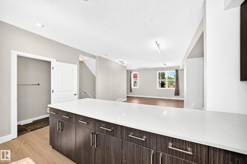 Modern kitchen island with a white countertop and wood-finish cabinetry, recessed ceiling lighting, and wood-finish flooring - #75 2803 James Mowatt Tr Sw, Edmonton, AB 