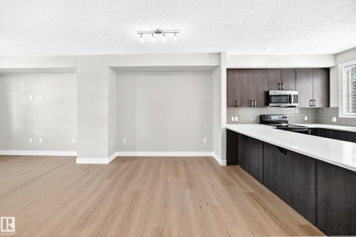 Wood-finish flooring throughout, track lighting, kitchen with dark wood-finish cabinetry, light-toned countertops, and stainless steel appliances - #75 2803 James Mowatt Tr Sw, Edmonton, AB 