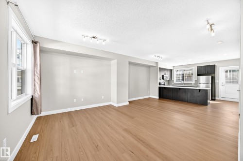 Open-concept living space with wood-finish flooring, recessed wall niche, and modern track lighting - #75 2803 James Mowatt Tr Sw, Edmonton, AB 