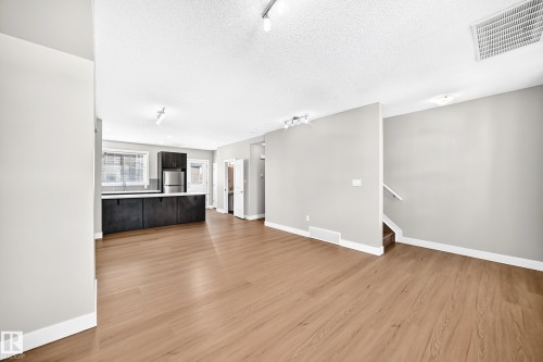 Open-concept living area with wood-finish flooring, a kitchen featuring dark wood cabinetry and stainless steel appliances, and a staircase with a white railing - #75 2803 James Mowatt Tr Sw, Edmonton, AB 