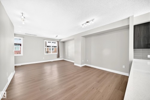 Wood-finish flooring, neutral wall tones, recessed wall feature, track lighting fixture, and a built-in countertop - #75 2803 James Mowatt Tr Sw, Edmonton, AB 