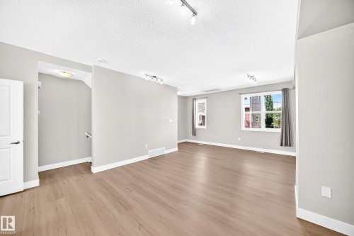Spacious room with wood-finish flooring, light grey painted walls, white trim, and multiple windows - #75 2803 James Mowatt Tr Sw, Edmonton, AB 