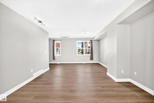 Spacious room featuring wood-finish flooring, light gray walls, white trim, and multiple windows - #75 2803 James Mowatt Tr Sw, Edmonton, AB 