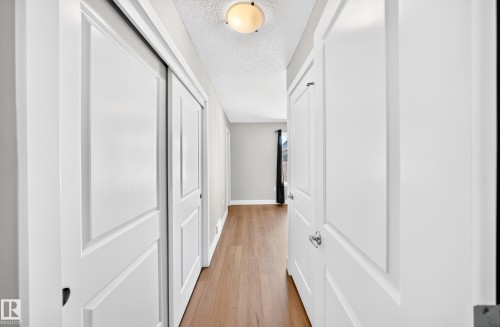 Hallway with wood-finish flooring and multiple white paneled doors - #75 2803 James Mowatt Tr Sw, Edmonton, AB 
