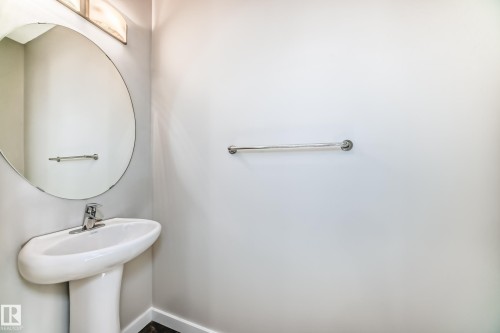 Pedestal sink with chrome faucet, circular mirror, and wall-mounted towel bars - #75 2803 James Mowatt Tr Sw, Edmonton, AB 
