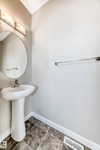 Pedestal sink with chrome faucet, circular wall-mounted mirror, and overhead vanity lighting - #75 2803 James Mowatt Tr Sw, Edmonton, AB 