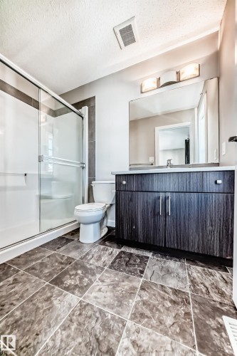 Tiled flooring, glass-enclosed shower with sliding door, wood-finish vanity with countertop, and large wall mirror - #75 2803 James Mowatt Tr Sw, Edmonton, AB 