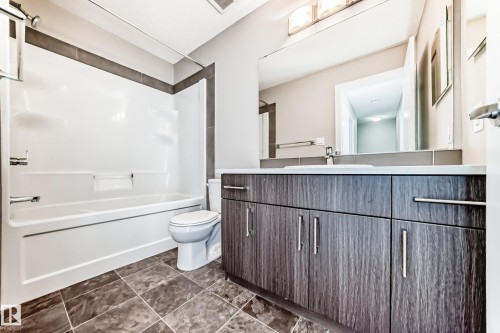 Contemporary bathroom featuring a wood-finish vanity with ample storage, a built-in bathtub with shower, and large format floor tiling - #75 2803 James Mowatt Tr Sw, Edmonton, AB 