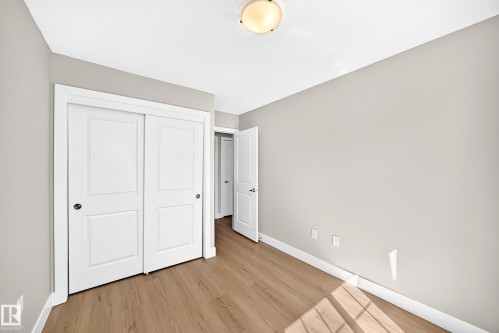 Wood-finish flooring, light grey walls, and a white sliding closet door - #75 2803 James Mowatt Tr Sw, Edmonton, AB 