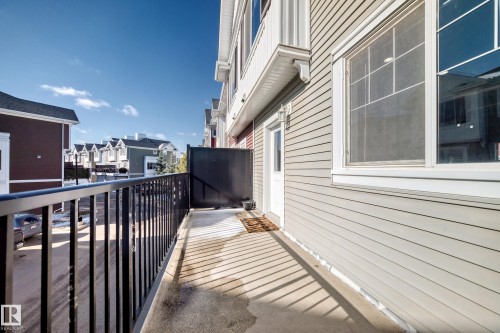Concrete balcony with black metal railings, light-colored horizontal siding, and a white entrance door - #75 2803 James Mowatt Tr Sw, Edmonton, AB 