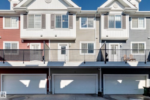 Multi-story townhouse exterior featuring a gabled roofline, vinyl siding, a private balcony with black railings, and an attached garage with a white sectional door - #75 2803 James Mowatt Tr Sw, Edmonton, AB 