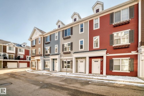 Townhome exterior featuring multiple dormer windows, decorative window boxes, shutters, and white entry doors - #75 2803 James Mowatt Tr Sw, Edmonton, AB 