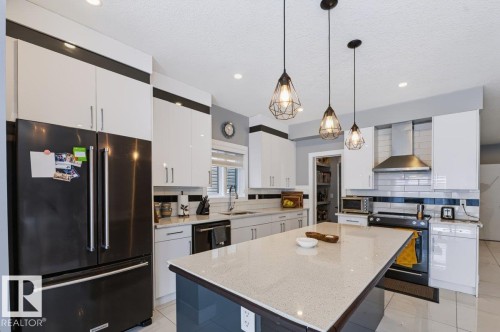 Kitchen featuring a central island with a light-toned countertop, pendant lighting, stainless steel appliances, white cabinetry, and a subway tile backsplash - 527 Merlin Landing Nw, Edmonton, AB - Indoor Photo Showing Kitchen With Double Sink With Upgraded Kitchen