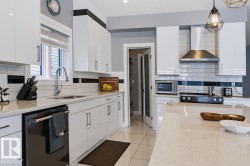 Modern kitchen featuring white glossy cabinetry, light-toned countertops, a stainless steel range hood, subway tile backsplash, and a glass-paneled pantry door - 