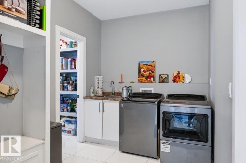 Laundry area featuring a utility sink, white base cabinetry with a stone-finish countertop, and a built-in storage bench with open shelving - 527 Merlin Landing Nw, Edmonton, AB - Indoor Photo Showing Laundry Room