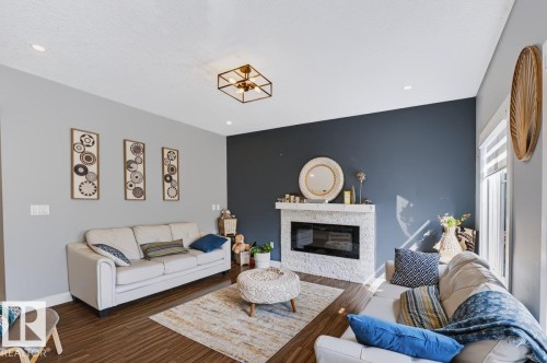 Recessed lighting, wood-finish flooring, a contemporary ceiling fixture, a built-in fireplace with a textured surround, and a large window with blinds - 527 Merlin Landing Nw, Edmonton, AB - Indoor Photo Showing Living Room With Fireplace