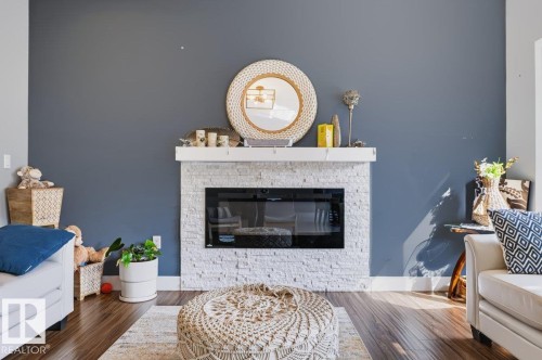 Modern fireplace with a stacked stone surround, dark wood-finish flooring, and a contrasting accent wall - 527 Merlin Landing Nw, Edmonton, AB - Indoor Photo Showing Living Room With Fireplace