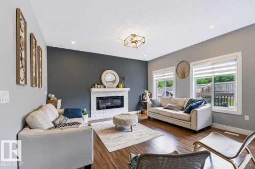 Living area featuring wood-finish flooring, a contemporary fireplace with a white stone surround, two large windows, and recessed lighting - 527 Merlin Landing Nw, Edmonton, AB - Indoor Photo Showing Living Room With Fireplace