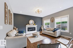 Living area featuring wood-finish flooring, a contemporary fireplace with a white stone surround, two large windows, and recessed lighting - 
