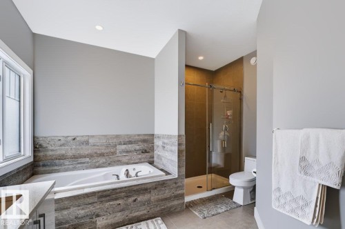 Built-in bathtub with wood-finish paneling, glass-enclosed shower, neutral wall paint, and recessed lighting - 527 Merlin Landing Nw, Edmonton, AB - Indoor Photo Showing Bathroom