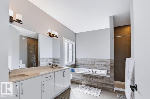 Dual vanity with integrated sinks and a large mirror, a built-in bathtub, a window with privacy glass, a walk-in shower with dark tile surround, and a light gray color palette - 527 Merlin Landing Nw, Edmonton, AB - Indoor Photo Showing Bathroom