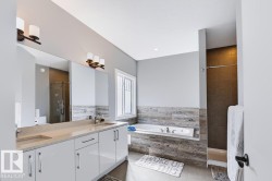 Dual vanity with integrated sinks and a large mirror, a built-in bathtub, a window with privacy glass, a walk-in shower with dark tile surround, and a light gray color palette - 