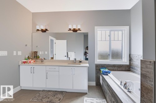 Double vanity with two integrated sinks, expansive mirror, contemporary light fixtures, built-in bathtub, and window with privacy glass - 527 Merlin Landing Nw, Edmonton, AB - Indoor Photo Showing Bathroom