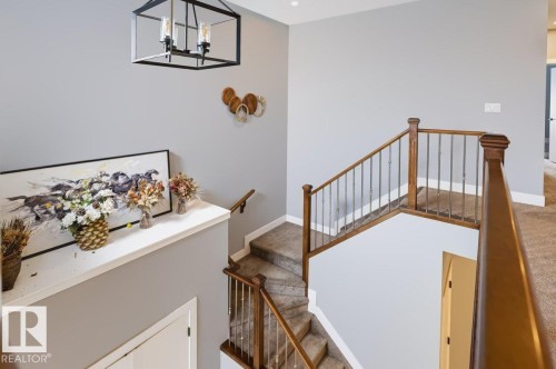 Staircase featuring wood railings with metal balusters, carpeted treads, and a contemporary chandelier - 527 Merlin Landing Nw, Edmonton, AB - Indoor Photo Showing Other Room