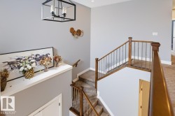 Staircase featuring wood railings with metal balusters, carpeted treads, and a contemporary chandelier - 