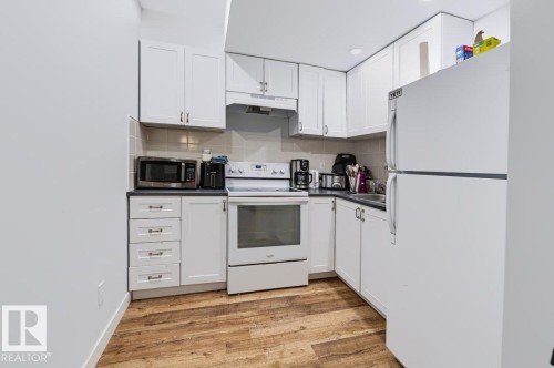 White cabinetry with ample storage, dark countertops, wood-finish flooring, and a tiled backsplash - 527 Merlin Landing Nw, Edmonton, AB - Indoor Photo Showing Kitchen