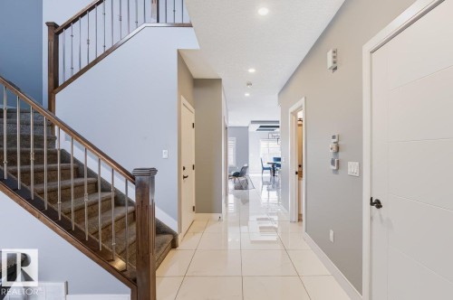 Staircase with wood newel posts and metal spindles, carpeted treads, white tile flooring, recessed ceiling lighting, and white paneled doors - 527 Merlin Landing Nw, Edmonton, AB - Indoor Photo Showing Other Room
