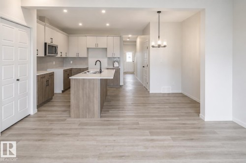 Kitchen featuring two-tone cabinetry, a central island with an integrated sink, and stainless steel appliances - 219 157 Avenue Ne, Edmonton, AB - Indoor Photo Showing Kitchen