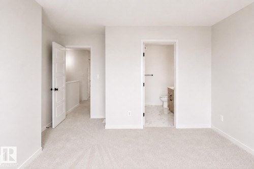 Plush carpeting, a paneled interior door, and a full bathroom with marble-finish flooring and a wood-finish vanity - 219 157 Avenue Ne, Edmonton, AB - Indoor Photo Showing Other Room