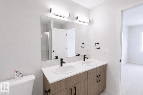 Dual vanity with wood-finish cabinetry, white countertop, and matte black fixtures - 219 157 Avenue Ne, Edmonton, AB - Indoor Photo Showing Bathroom