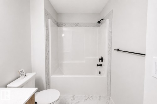 Bathtub and shower combination with matte black fixtures, framed by marble-look tile surround and complementing floor tile - 219 157 Avenue Ne, Edmonton, AB - Indoor Photo Showing Bathroom