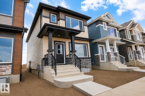 Two-story residence featuring light-colored siding with dark trim accents, a covered front entry with stone-clad columns, and a concrete pathway leading to the entrance - 219 157 Avenue Ne, Edmonton, AB - Outdoor With Deck Patio Veranda With Facade