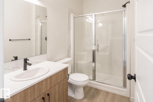 Wood-finish vanity with an integrated sink and matte black faucet, glass-enclosed shower with a built-in bench, and light wood-finish flooring - 219 157 Avenue Ne, Edmonton, AB - Indoor Photo Showing Bathroom